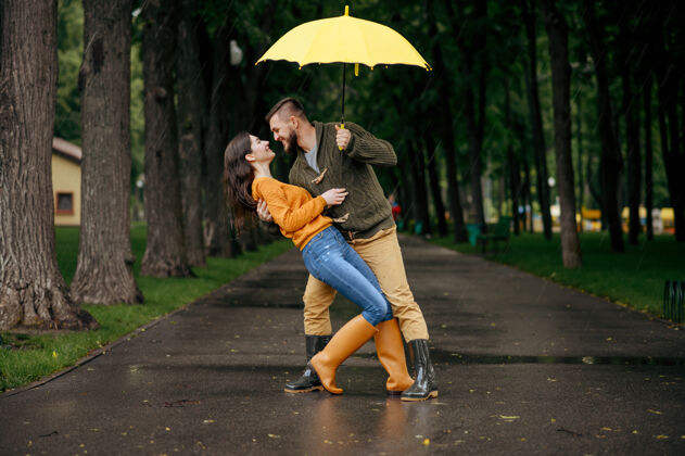 年轻夏日雨中公园里快乐的情侣跳舞戴曼雨中的女人在雨伞下拥抱 散步路上的浪漫约会 巷子里的潮湿天气户外人一起