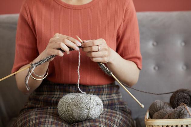 休闲服坐在沙发上为自己织温暖羊毛围巾的女人的特写镜头设备缝纫针特写
