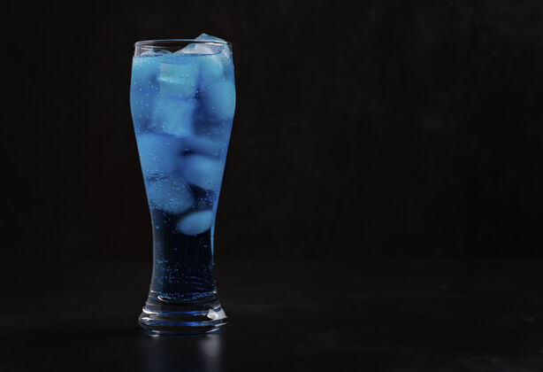 饮料高玻璃杯里放着冰块的蓝色鸡尾酒站在黑暗中蓝色鸡尾酒热量酒精鸡尾酒