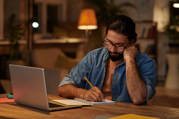 设计师一个留着大胡子的正经商人坐在笔记本电脑前的笔记本上做笔记办公室眼镜小企业