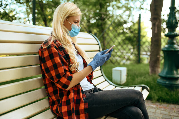 医药戴着面具的年轻女子坐在公园的长椅上 隔离女性人在流行期间行走 保健和保护 流行的生活方式检疫社会距离户外