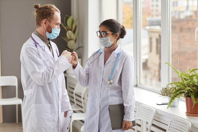 医务室两个戴着口罩的医务人员站在走廊上互相问候健活方式团队医学