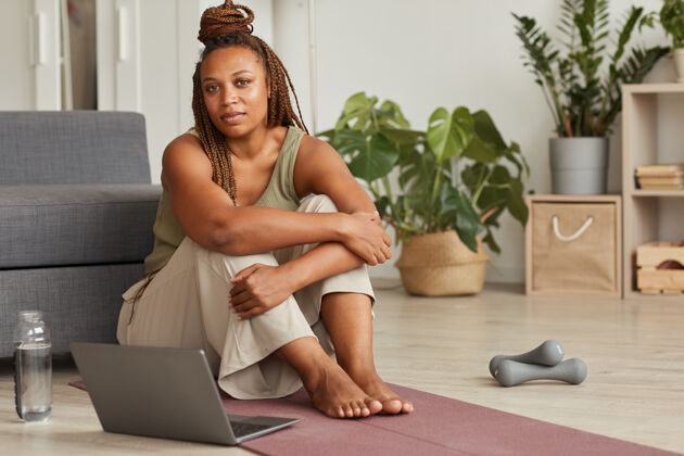 技术照片中的非洲妇女坐在地上 拿着笔记本电脑 在家里进行体育训练前在线观看体育锻炼非裔美国人笔记本电脑放松