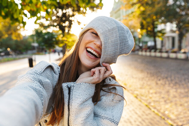 人一位穿着秋衣戴秋帽的美丽年轻女子在户外散步 自拍移动时尚微笑