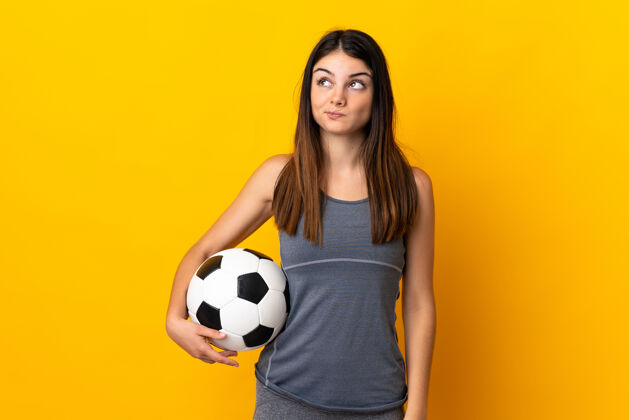 女孩一个年轻的足球运动员被隔离在黄色的墙上 抬头望去比赛运动员游戏