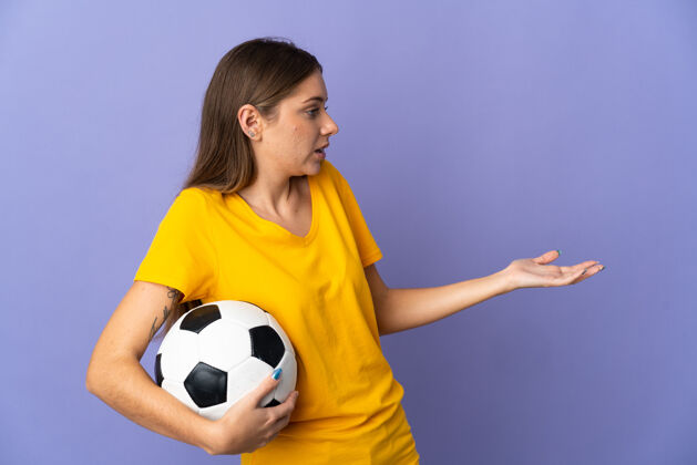 女子年轻的立陶宛足球运动员女子孤立在紫色背景与惊喜的表情 而一边看球成人青年