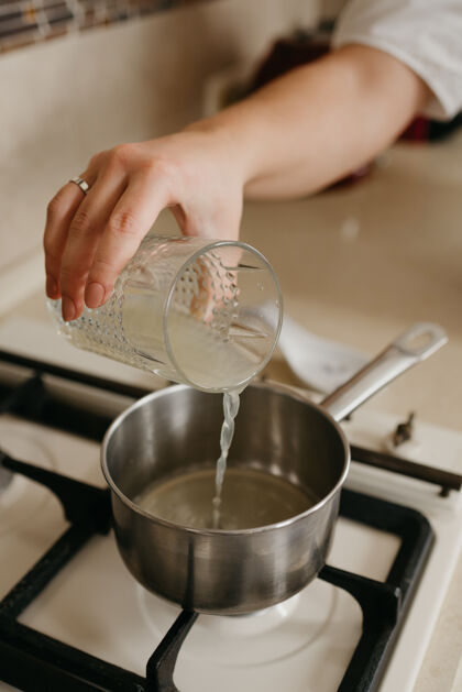 准备一个女人的手把新鲜的柠檬汁从玻璃杯倒到煤气炉上的平底锅里自制柠檬杯子
