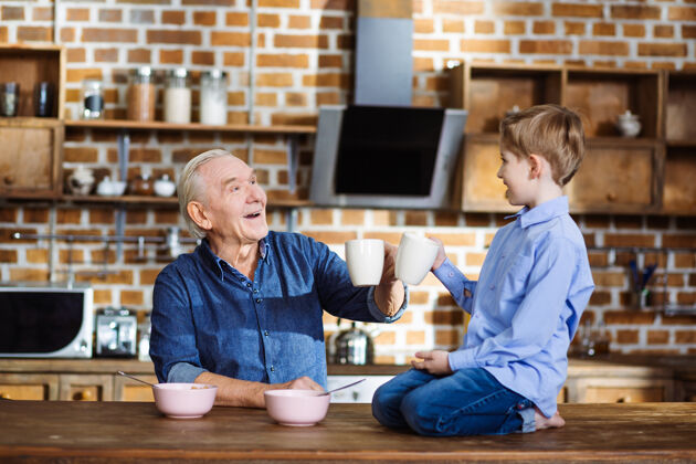 成熟快乐的小男孩一边喝茶一边和爷爷吃早餐桌子享受食物