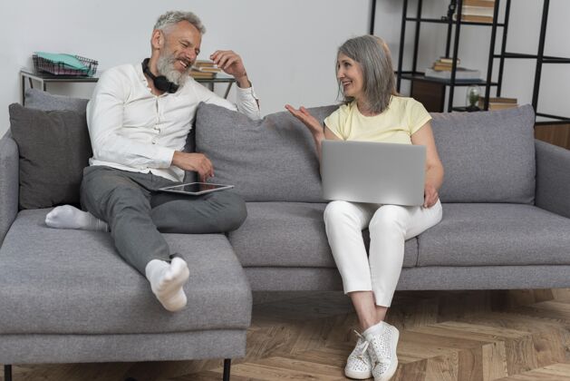水平资深男女在家沙发上使用笔记本电脑和平板电脑书房学习老年夫妇