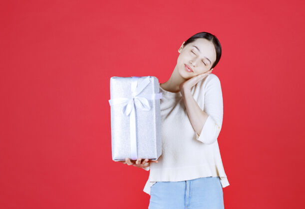 生日快乐的美女拿着礼品盒站在红墙上快乐人脸