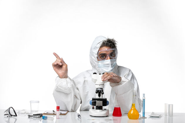 专业穿防护服戴口罩的男医生用显微镜对着白色的套装医生男医生
