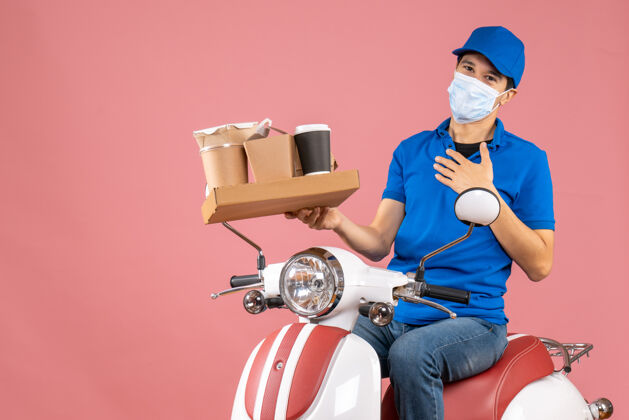 摩托车正面图是戴着帽子戴着面具的男性送货员坐在滑板车上 在桃色背景下送货面具机器人