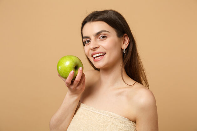 身体特写黑发半裸完美皮肤的女人 裸妆把苹果隔离在米色粉彩墙上饮食有机自然