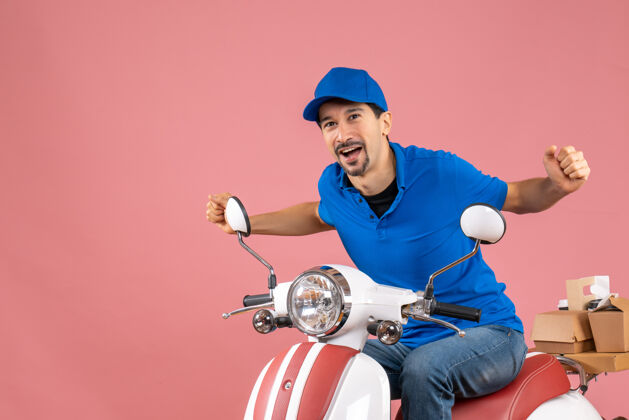 人物前视图的快乐送货员戴着帽子坐在粉彩桃色背景的踏板车上高尔夫球手运动员头盔
