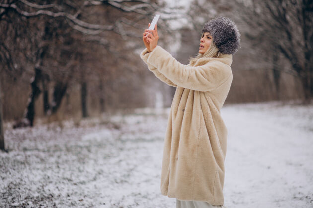 女性穿着冬衣的女人走在满是雪的公园里打电话寒冷帽子旅程
