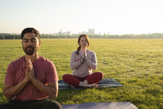 锻炼男人和女人在户外瑜伽垫上冥想的正面图思想专注草