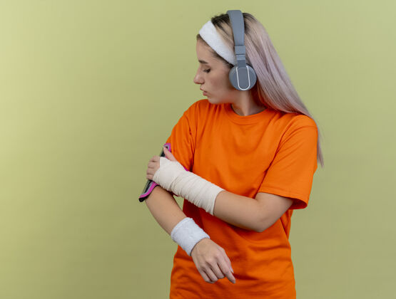 臂带自信的年轻白种人戴着耳机戴着头带和腕带 手放在手机袖标上运动年轻橄榄
