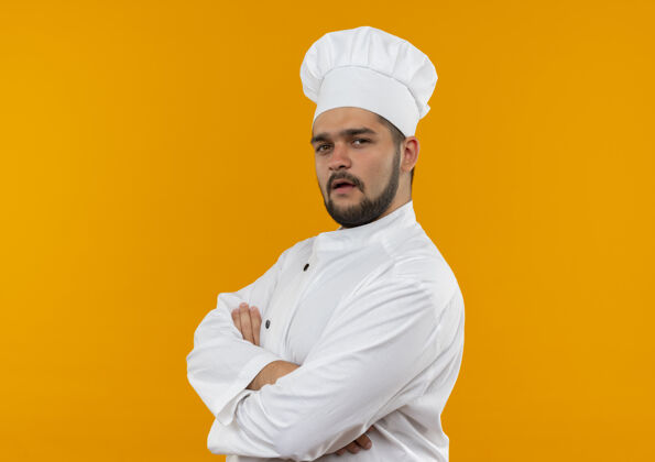 站立自信的年轻男厨师身着厨师制服站在侧视图中 封闭的姿势隔离在橙色的墙上 留有复制空间制服侧写视野
