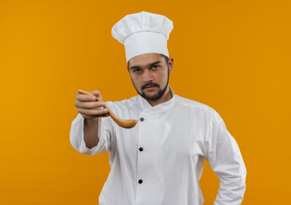 制服自信的年轻男厨师身着厨师制服 在橙色的墙上伸出汤匙自信男性勺子