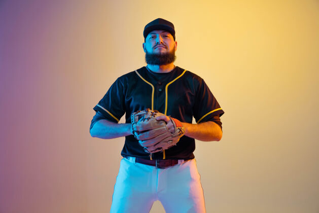 球棒球运动员 穿着黑色制服的投手在霓虹灯下的梯度背景上练习和训练运动比赛头盔