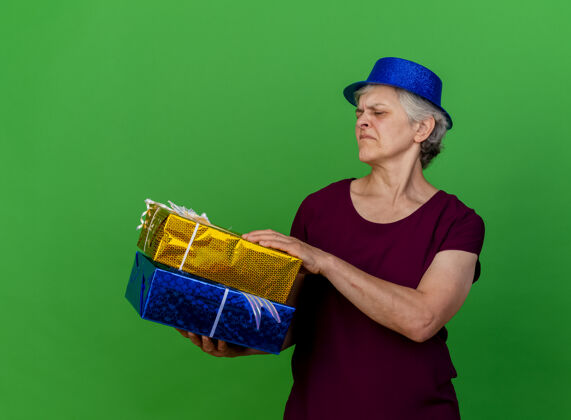 老人未出租的老妇人戴着聚会的帽子拿着礼物盒看绿色不愉快女人聚会