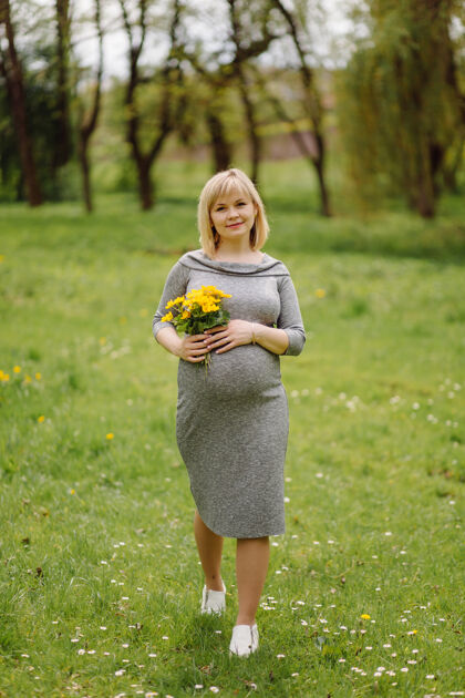 爱年轻的金色孕妇身着灰色连衣裙 怀孕的女孩在春天散步 母性观念怀孕母亲服饰