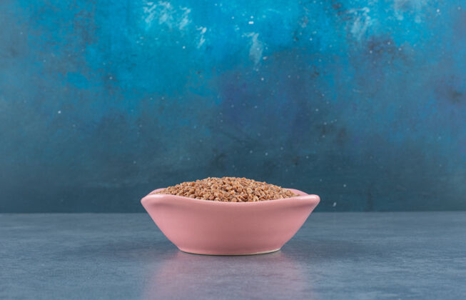 谷物荞麦堆在一个粉红色的碗里 堆在蓝色的地上生的谷类烹饪