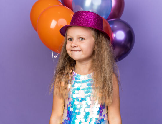 小兴奋的金发小女孩 戴着紫色派对帽 站在紫色的墙上 氦气球与复制空间隔离开来站孤立帽子