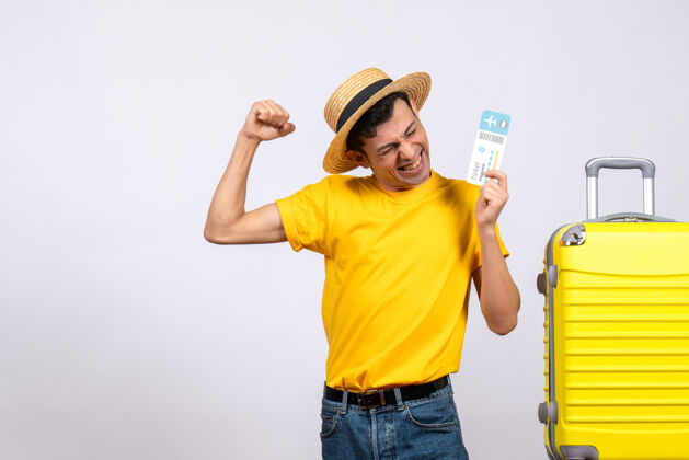 前面正面图：穿着黄色t恤的年轻人站在黄色手提箱旁 手里拿着车票 表达他的幸福黄色快车手提箱