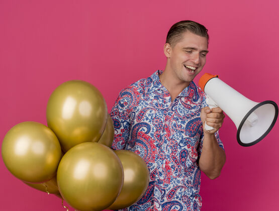 抱着快乐的年轻人一边看一边穿着五颜六色的衬衫拿着气球 一边用扬声器讲话 粉红色的脸上孤立着欢乐穿派对