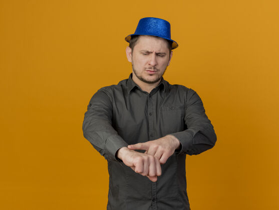 穿严格的年轻人戴着蓝色帽子的党脚上的橙色手表时钟手势孤立蓝色橙色帽子