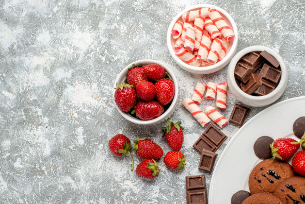 巧克力顶视图饼干草莓和圆形巧克力放在白色盘子上 碗里放着糖果草莓巧克力放在灰白色的地面上糖果浆果农产品