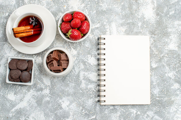 茶顶视图碗草莓和巧克力肉桂茴香籽茶和笔记本在灰白色的地面上盘子笔记本浆果