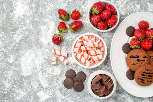 草莓顶视饼干草莓和圆形巧克力在椭圆形盘子碗糖果草莓巧克力在右边的灰白色的桌子新鲜食物浆果