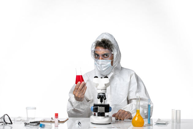 外套正面图：男医生穿着防护服 戴着口罩 拿着装有红色溶液的烧瓶 背景是白色的健康大流行病毒大流行实验室外套防护