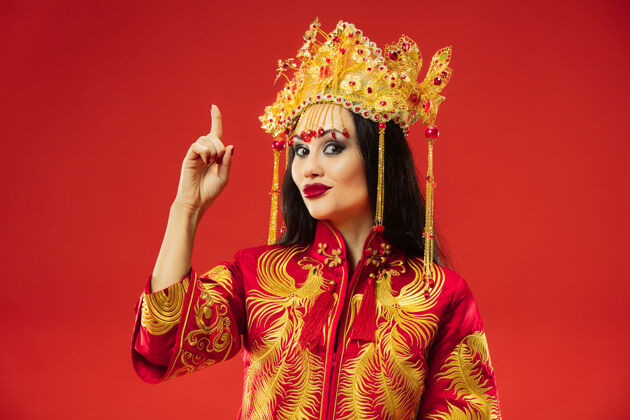 脸中国传统的优雅女子在摄影棚的红色背景美丽的女孩穿着民族服装中国新年 优雅 优雅 表演者 表演 舞蹈 女演员 情感概念肖像惊奇女性