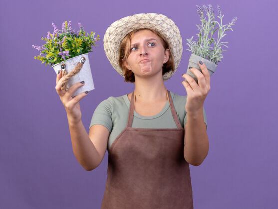 年轻困惑的年轻斯拉夫女园丁戴着园艺帽 拿着紫色的花盆看花花困惑帽子