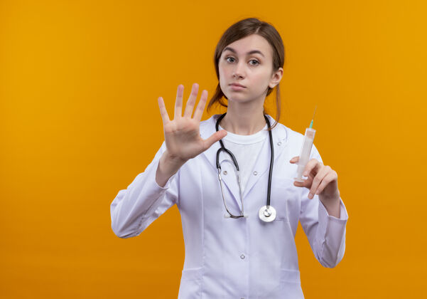 五一位面容严肃的年轻女医生 穿着医用长袍 手持注射器 手持听诊器 在橙色的空白处和复印处展示了五个橙色注射器长袍