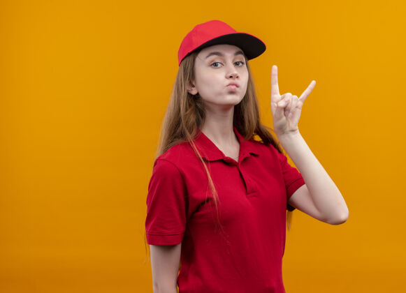 女孩自信的年轻送货女孩穿着红色制服在孤立的橙色空间做摇滚标志与复制空间自信制服橙色