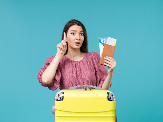 前面前景度假中的女人拿着她的钱包和票在浅蓝色背景上旅行度假旅行的女人夏天的海光旅程蓝色
