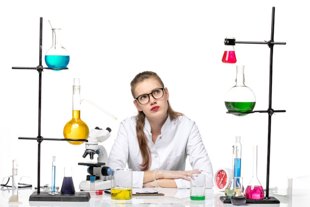 医学前视图：身着医疗服的女化学家在桌子前拿着浅白背景上的溶液大流行化学冠状病毒女化学家成人实验室