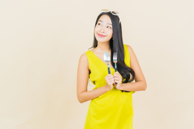 女孩画像美丽的亚洲年轻女子在彩色墙上用勺子和叉子微笑亚洲人木头情感