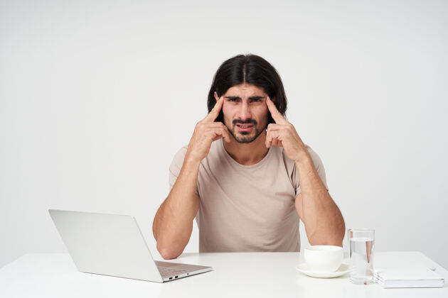 胡须紧张的男性 疲惫的商人 黑头发和胡须办公室观念坐在工作场所头痛按摩太阳穴隔着白墙表情笔记本电脑帅气