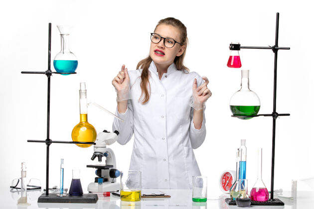 女化学家前视图身着医疗服的女化学家站在白色背景上的不同溶液前化学大流行的冠状病毒支架专业实验室