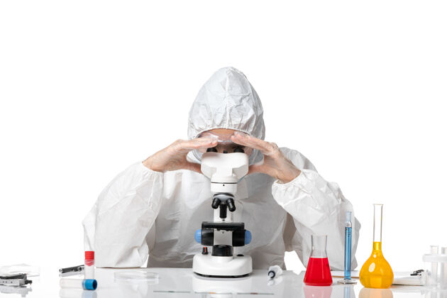 健康正面图女医生穿着防护服 戴口罩 用显微镜观察白色背景病毒大流行健康病毒套装病毒人