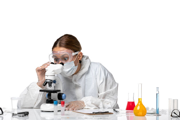 外套正面图女医生穿着防护服 戴着口罩 用显微镜观察白色背景的健康冠状病毒大流行使用视图实验室外套