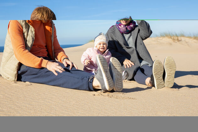 女性快乐的父母和甜蜜的小宝宝穿着暖和的衣服 在海上度过闲暇时光 一起坐在沙滩上家庭时间大衣