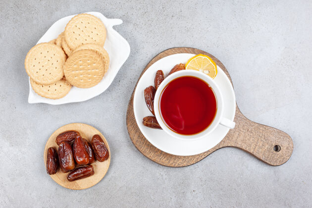 茶碟一盘曲奇饼和一小堆枣子放在一杯茶旁边 茶碟上放着一些枣子放在木板上 放在大理石表面香喷喷早餐辣味十足