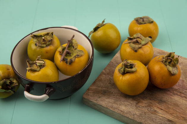 视野木制厨房板上橙色圆形柿子果实的俯视图 蓝色木桌上的碗上有柿子果实水果橘子顶部