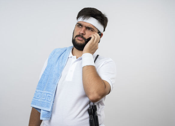 说话思想年轻的运动型男子一边看一边戴着头带和手环与毛巾和跳绳在肩上讲电话隔离在白色的墙壁与复制空间肩膀头带男人
